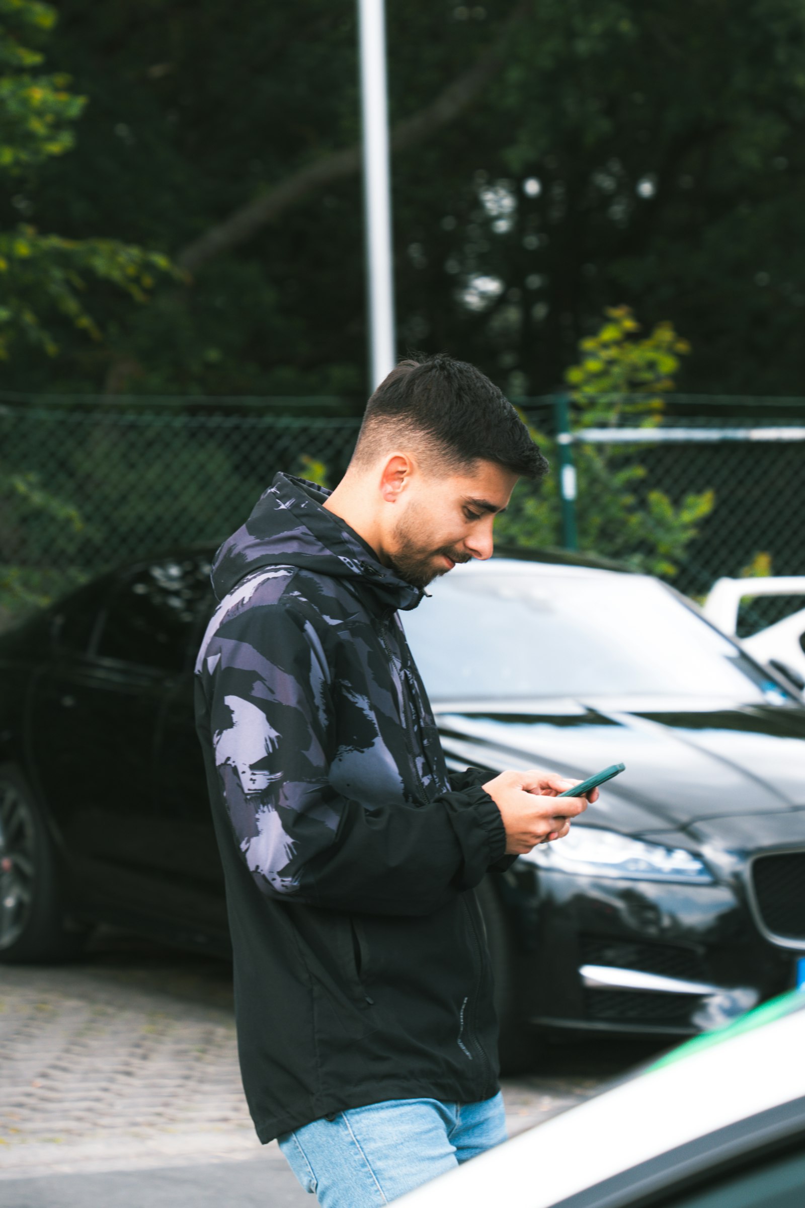A car owner checking his phone next to his car in a parking lot